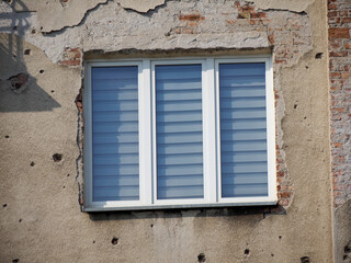 Modern Window with Horizontal Blinds on Damaged Building Facade Showing War Remnants