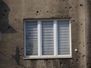 Modern Window with Shutters on War-Damaged Building Facade with Bullet Hole History