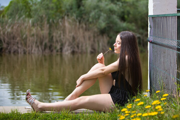 Young, dark and beautiful woman dressed in black holds in her hand a yellow flower and smells it,...