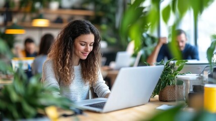 Smiling young woman works on laptop in a modern, plant-filled co-working space, surrounded by colleagues and greenery. : Generative AI