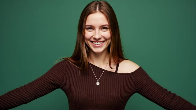 A young woman stands against a solid green background, smiling brightly with arms outstretched