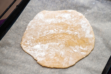 Flat honey dough crust on parchment paper, ready for baking on a baking sheet in the oven