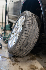 Car Tire Change Process with Vehicle Lifted on Jack During Seasonal Maintenance. Close-up of Tire on Alloy Wheel Being Removed or Installed with Professional Hydraulic Equipment Visible in Background