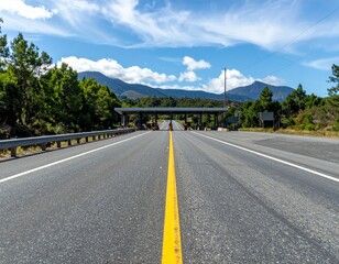 Fototapeta premium Scenic Roadway with Toll Booth Surrounded by Lush Greenery and Mountains