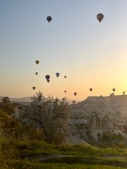 Colorful hot air balloons fill the sky as the sun rises over the unique rock formations of Cappadocia in Goreme, Turkey. Visitors enjoy the breathtaking scenery