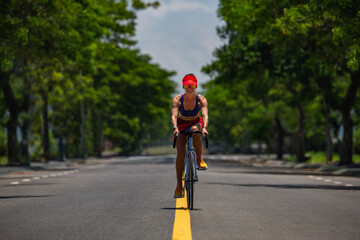 Fototapeta premium Fit woman cycling on empty road in summer, front view..