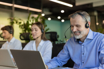 Smiling friendly handsome middle aged male call centre operator. Colleagues on the background