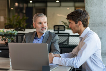 Two business people discussing work together using a tablet in a modern office
