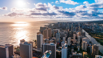 Fototapeta premium Waterscape of the Pacific Ocean reflecting the light of setting sun. Some boats sail by the ocean. Drone footage rising above the buildings of Waikiki, Honolulu, Hawaii, USA.