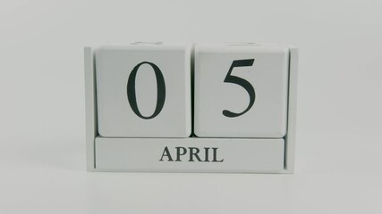 A hand flips a wooden calendar from April 5th to April 6th on a white background, representing the daily transition and passage of time