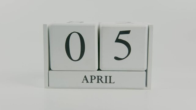 A hand flips a wooden calendar from April 5th to April 6th on a white background, representing the daily transition and passage of time