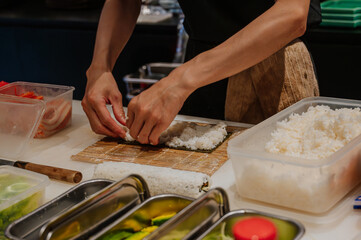 Chef's hand rolling up sushi on a bamboo mat.