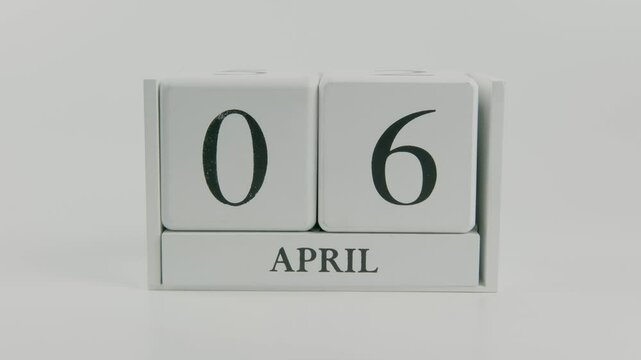 A hand flips a wooden calendar from April 6th to April 7th on a white background, visually marking the shift of days in a minimal and clean layout