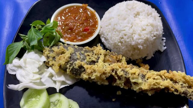 Pecel lele menu complete with fried catfish served with rice, cabbage leaves, sliced ​​cucumber and chili sauce ready to eat.