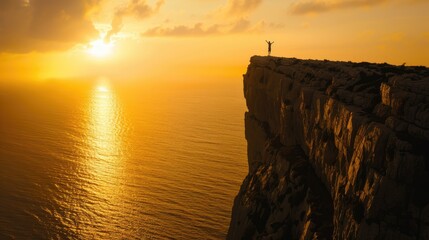 Silhouetted figure on clifftop at golden sunset over water.