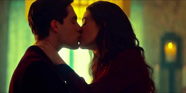 Young couple kissing in close-up, embracing with soft, warm lighting and dark background. Warm tones and profile views highlight intimacy, passion, and emotional connection in romantic moment.