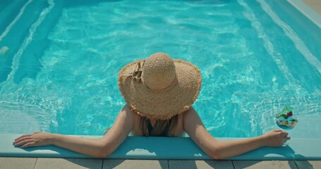 Young woman relaxing in a swimming pool with a cocktail, wearing a straw hat and enjoying a sunny summer day - Powered by Adobe
