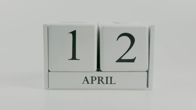 A hand flips a wooden calendar from April 12th to April 13th on a white background, visually capturing the movement of time and the rhythm of daily transitions