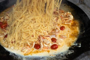 Spaghetti mit Scampis, Tomaten und Sahnesause in der Bratpfanne.