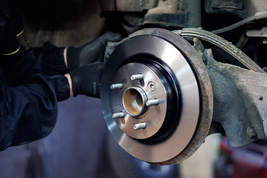 Mechanic replacing car brake disc in auto workshop, Close-up of a mechanic's hands installing a new brake disc on a vehicle during repair.