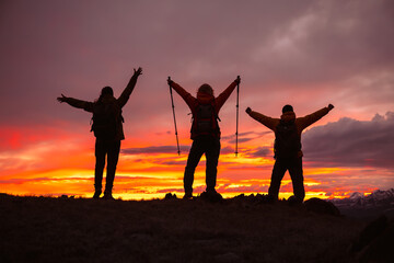 A small group of tourists celebrate reaching the top of a mountain against the backdrop of a colorful sunset