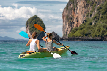 Two girls kayak across turquoise water to limestone island, Phi-Phi islands, Krabi province,...