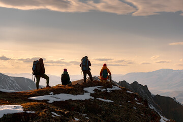 A group of tourists sits or stands on the top of a mount and looks at a mountain range on sunset © cppzone