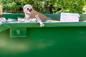 Anatomical skeleton model in a skip among the rubbish and trash