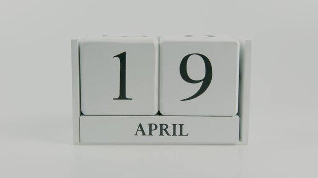 A hand flips a wooden calendar from April 19th to April 20th on a white background, illustrating the transition of time and the importance of staying on top of daily tasks and events