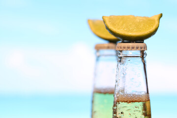 Bottled beer with lime against the sea. Close-up of a bottle of beer with a slice of lime, selective focus. Refreshing drink. Resort and recreation concept. Photo on the veranda of the bar