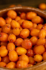 sea buckthorn berries in a wooden bowl on the table, defrosting ripe sea buckthorn berries to make a drink, side view