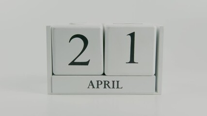 A hand flips a wooden calendar from April 21st to April 22nd on a white background, marking the ongoing passage of time, emphasizing organization, and the importance of timely scheduling and planning