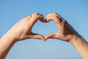 Female hands forming a heart shape against a clear blue sky