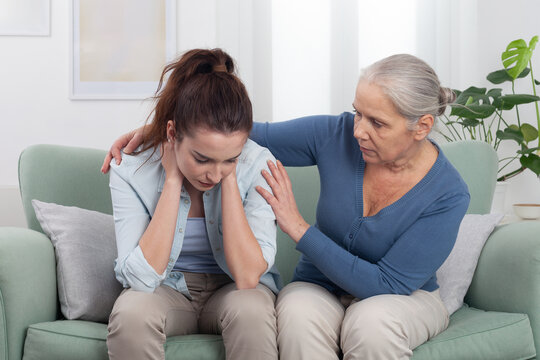 Caring elderly grandmother hugs and comforts her upset granddaughter at home. Emotional and touching family moment showing love, empathy, and intergenerational support during a difficult time