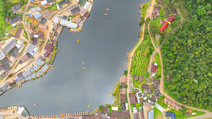 aerial top view of a lakeside village, showcasing a mix of rustic architecture, lush greenery, and boats scattered across the calm water. A harmonious blend of natural beauty and human settlement..