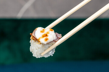 hand with wooden chopsticks taking sushi roll on a deep blue background. Asian restaurant menu. Copy space