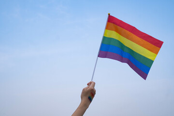 A hand waving a vibrant rainbow flag against a blue sky, symbolizing pride, diversity, and inclusivity. Perfect for celebrations and culture themes.