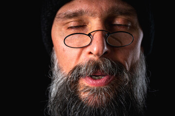 emotional of angry bearded man in glasses and knitted hat, growling at camera, grimacing. Dramatic...