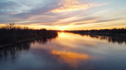 Fototapeta premium Serene sunrise over a calm river, reflecting the vibrant orange and pink hues of the dawn sky. Bare trees line the banks, creating a peaceful winter landscape. : Generative AI