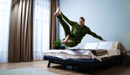 Joyful man leaps over bed in bright, sunlit bedroom. Playful energy fills the room, capturing the essence of youthful spirit and happiness indoors.
