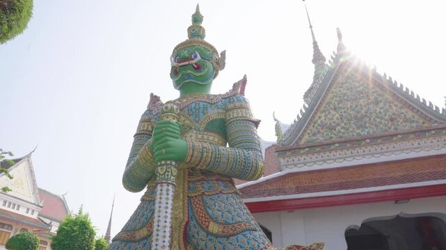 The iconic green giant statue (Thotsakan) standing guard in front of the ordination hall under bright sunlight at Wat Arun, Bangkok, Thailand.