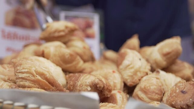 A close-up shot of freshly baked golden-brown curry puffs piled up on a tray at a local Thai street food market.