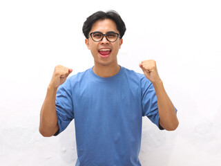 Naklejka premium Portrait of a cheerful young Asian man doing raised his fist with a happy smile on his face as a gesture of celebration