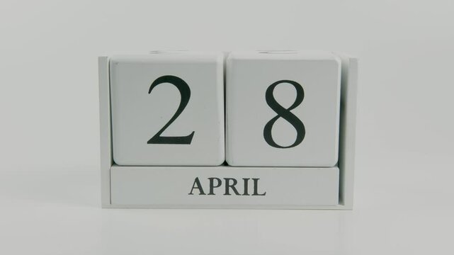 A hand flips a wooden calendar from April 28th to April 29th, marking the transition from one day to the next, with a white background emphasizing the passage of time