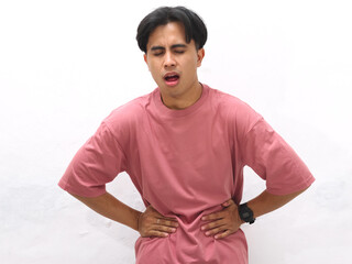 Unhealthy Young Asian man in a pink tshirt  holding his stomach in pain and sadness against a white...