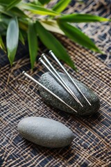 Acupuncture needles on a stone, nestled amidst bamboo and textured fabric