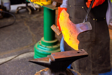 Blacksmith skillfully shapes glowing piece of metal with hammer while working in during axe making