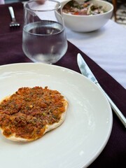 A small lahmacun — traditional Turkish flatbread topped with minced meat and herbs, served at an outdoor restaurant