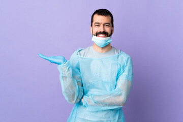 Surgeon man with beard with blue uniform over isolated purple background holding copyspace imaginary on the palm to insert an ad