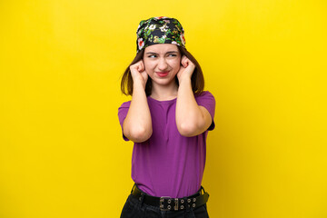 Young Ukrainian woman isolated on yellow background frustrated and covering ears